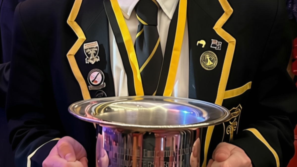 Student in a striped school blazer wearing custom school badges and enamel pins, holding a silver trophy