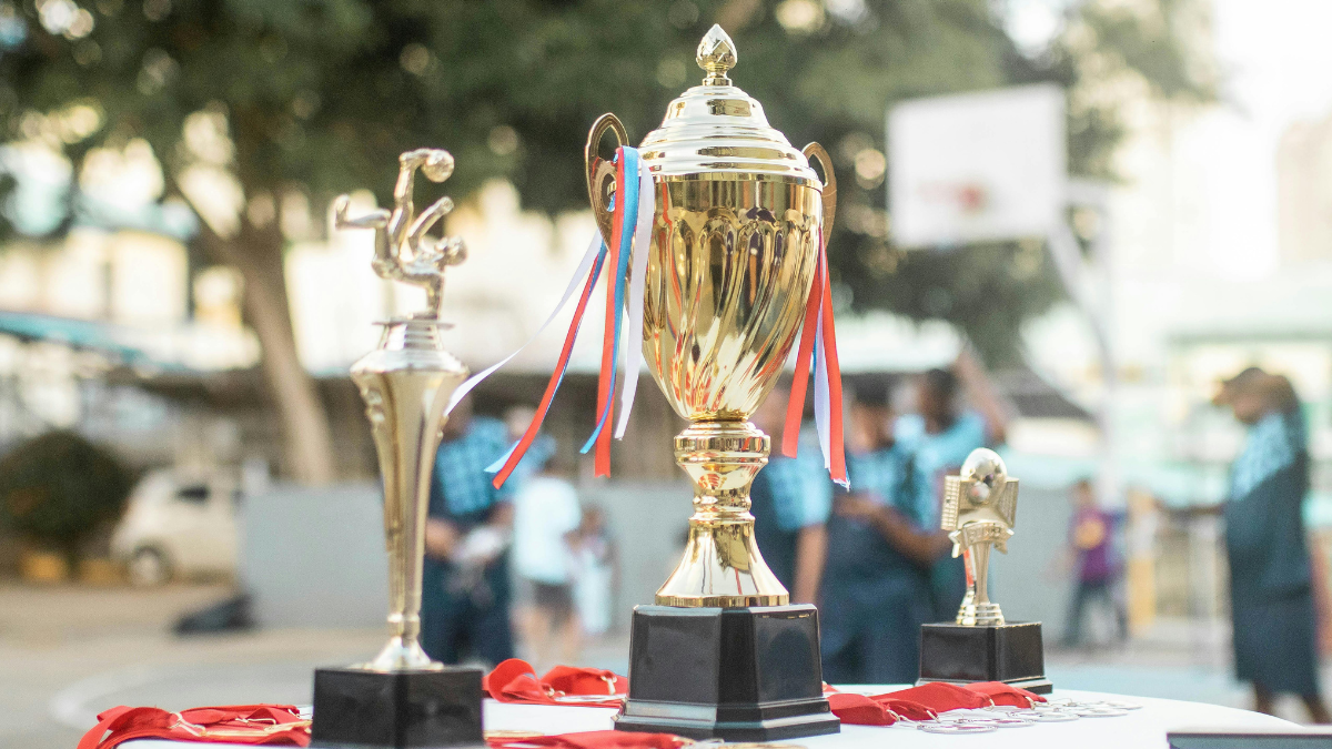 Gold sports club trophies and medals with red ribbons on a table at an outdoor prizegiving